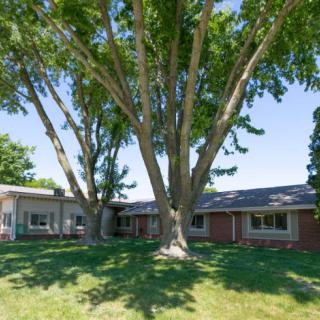 A brick house surrounded by lush trees and a well-maintained lawn.
