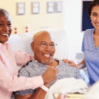 A patient is smiling while receiving care from a nurse and being supported by a family member in a hospital setting.