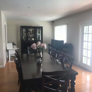 A well-lit dining room with a dark wooden table and chairs, decorated with flowers in a vase.