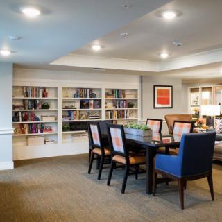 A cozy meeting area with a dining table surrounded by chairs, bookshelves filled with books, and artwork on the wall.