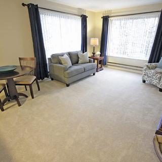 A cozy living room with furniture, including a sofa and armchair, complemented by large windows with curtains.