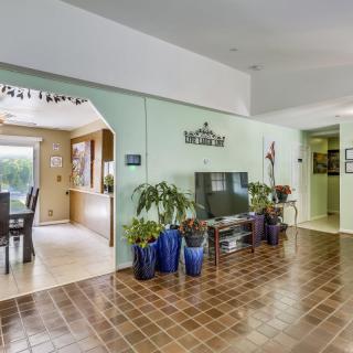 A cozy living room with tile flooring, featuring a television and potted plants, opening into a dining area.