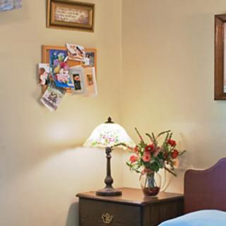 A cozy bedroom corner featuring a nightstand with a lamp and flowers, complemented by a photo board on the wall.