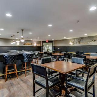 An empty restaurant interior with tables, chairs, and bar stools under warm lighting.
