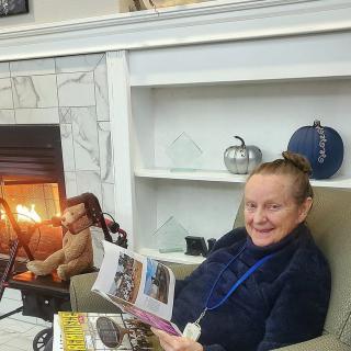 A woman sitting in a cozy chair by the fireplace, reading a magazine.