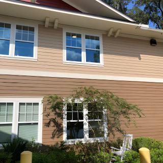 A two-story residential building with several windows, a plant in front, and a rocking chair by the window.