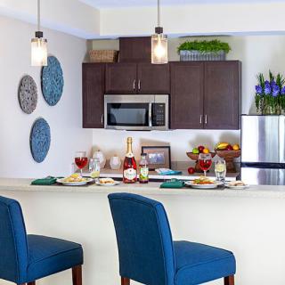 A modern kitchen with a dining area, featuring blue bar stools and elegant pendant lighting.