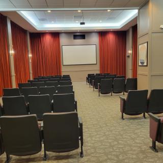 An empty theater room with arranged seats and a projection screen.