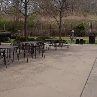 A quiet outdoor seating area featuring empty tables and chairs surrounded by trees.
