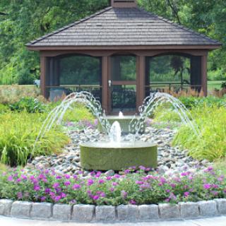 A serene garden featuring a central fountain and a gazebo, surrounded by vibrant flowers.
