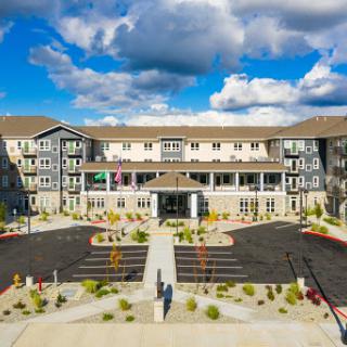 A modern residential building showcasing a well-maintained courtyard and ample parking, set against a backdrop of fluffy clouds.