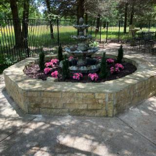 A decorative garden fountain surrounded by flowers and a stone wall.