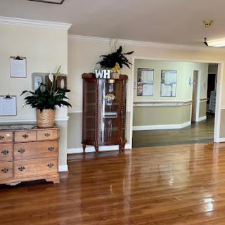 A spacious and inviting living area featuring polished wooden floors, a vintage dresser, and decorative plants.