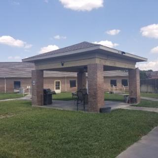 A spacious outdoor pavilion surrounded by manicured grass and a clear blue sky.