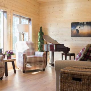 A cozy living room with wooden walls, featuring a piano, armchairs, and rattan furniture.