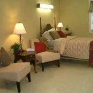 A cozy bedroom with a neatly made bed, comfortable chairs, and warm lighting.