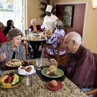 Elderly individuals enjoying a meal together at a restaurant, served by a chef.