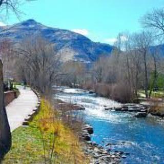 A scenic view of a river flowing alongside a mountain, with bare trees lining a pathway.