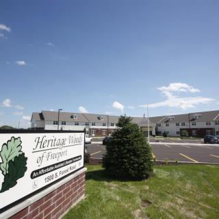 A view of an apartment complex with a sign reading 'Heritage Village of Waterville' under a clear blue sky.