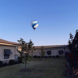A hot air balloon floats gently in the blue sky above a serene courtyard.