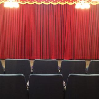 An empty theater with red curtains and rows of seats facing the stage.
