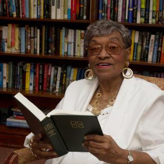 An elderly woman reading a book in a library.