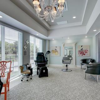 A modern salon interior with stylish chairs, a chandelier, and large windows letting in natural light.