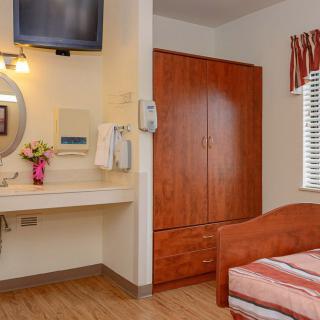 A cozy bedroom with a wooden wardrobe, a bed, and a vanity area featuring a sink and mirror.