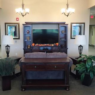 A cozy living room setup featuring a large wooden entertainment center with a television, flanked by two table lamps and potted plants.