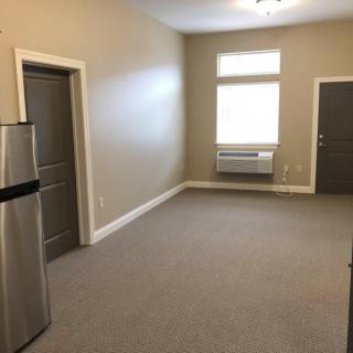 An empty apartment living space with a fridge and air conditioner.