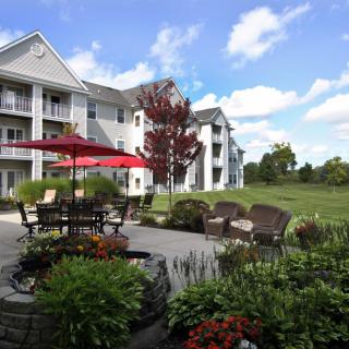 A scenic view of a residential apartment complex with a well-maintained patio and garden, featuring outdoor seating and vibrant landscaping under a blue sky.