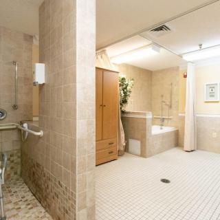A spacious, accessible bathroom with a tiled floor, featuring a shower area and a bathtub equipped with grab bars.