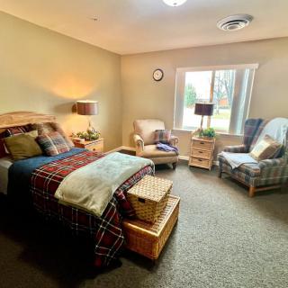 A cozy bedroom with a neatly made bed, armchairs, and warm lighting.
