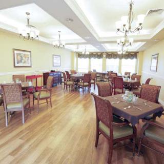 A well-lit dining room with multiple tables and chairs, featuring chandeliers and hardwood flooring.