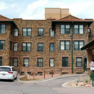 A view of a stone apartment building featuring multiple windows and a parking area in front.