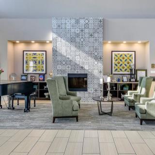 A modern lobby featuring a cozy seating area with a fireplace, piano, and decorative artwork.