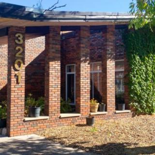 A brick building with the address number 3201, featuring a row of large windows and surrounded by plants.