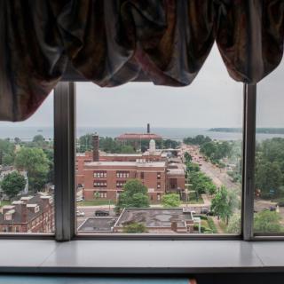 A view from a window overlooking an urban landscape with trees and historical buildings under a cloudy sky.