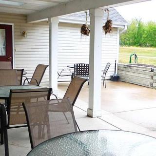 A covered patio with outdoor seating and glass tables, overlooking a backyard.