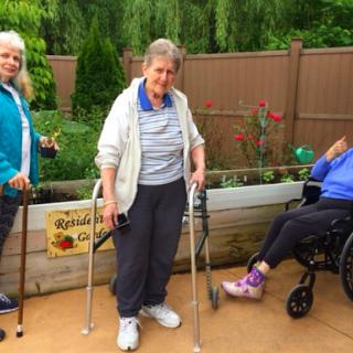 Three senior women enjoying time outdoors, with one using a wheelchair and two utilizing walking aids.