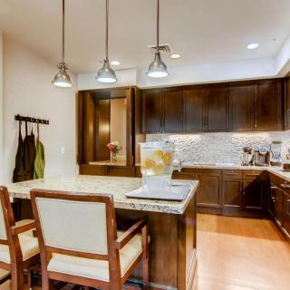 A modern kitchen with wooden cabinets, pendant lighting, and a small dining area with bar stools.