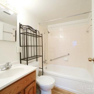 A small bathroom featuring a bathtub with a curtain, toilet, sink with a mirror above, and a black metal shelving unit.