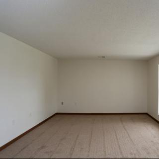 An empty room with carpeted flooring, white walls, and natural light coming through a window.