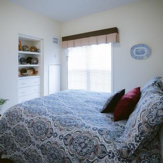 A cozy bedroom with patterned bedding and decorative pillows, featuring shelves and a large window.