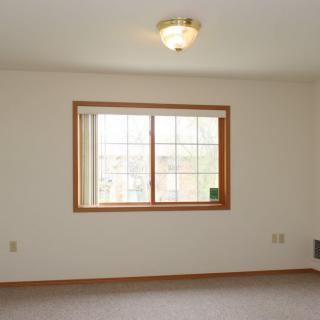 An empty room with a large window and a ceiling light fixture, showcasing neutral decor.