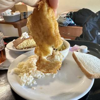A plate of fried fish served with coleslaw and a slice of bread.