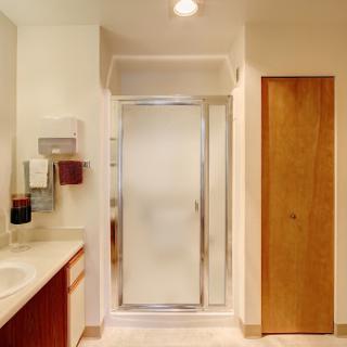 A well-lit bathroom featuring a shower enclosure, vanity, and a wooden door.