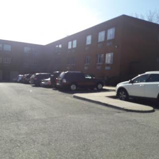 A view of a residential building with parked cars in the foreground on a sunny day.