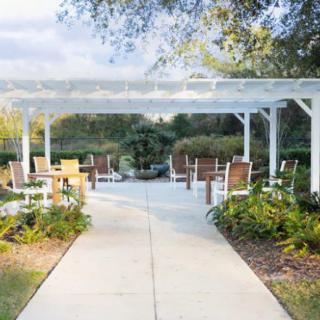 A tranquil outdoor garden area featuring a pergola with seating and lush landscaping.