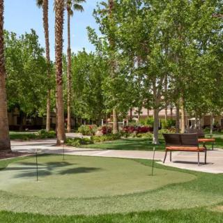 A serene park landscape featuring a small putting green surrounded by trees and benches.